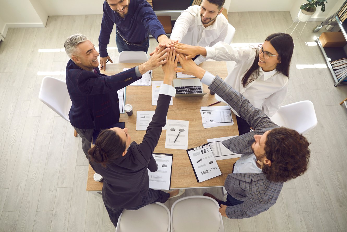 Happy Sales Team Standing around an Office Table and Giving Each Other a High Five